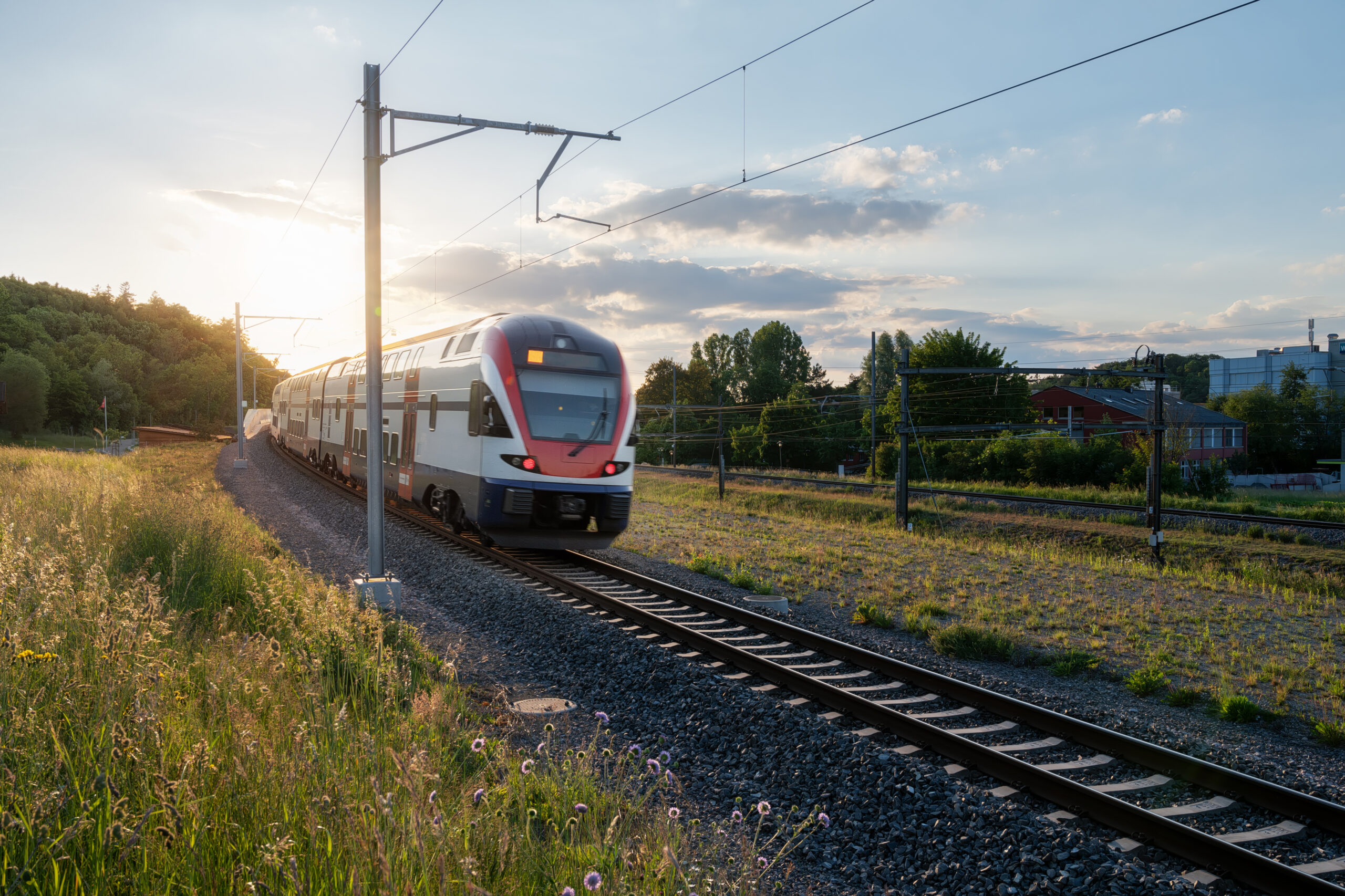 Nahverkehrszug fährt bei Sonnenuntergang durch Landschaft.